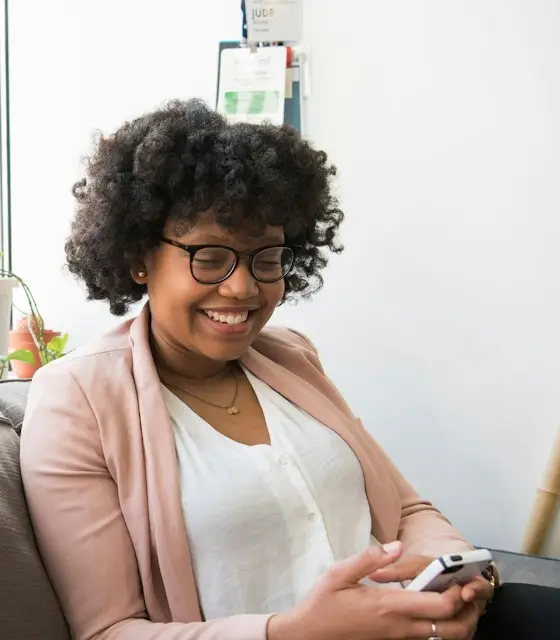 A smiling woman relaxing on a sofa, using the TherapyDock app on her phone