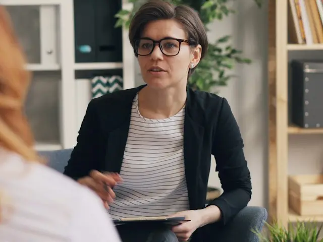A therapist with a notebook listening to a client in her office